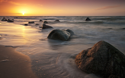 Golden sunset light shining upon the rocks on the beach Wallpaper