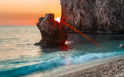 Red sun rising between the rocky ocean shore wallpaper