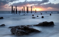 Wooden pillars standing tall towards the ocean sunset wallpaper 2560x1600 jpg